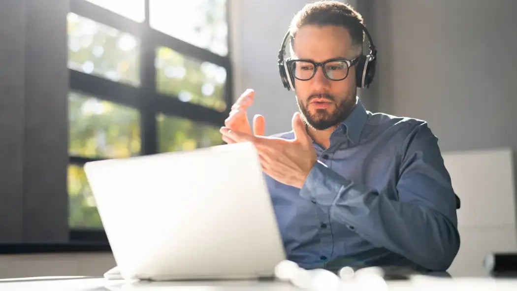  a man sat at a laptop with headphones on and talking